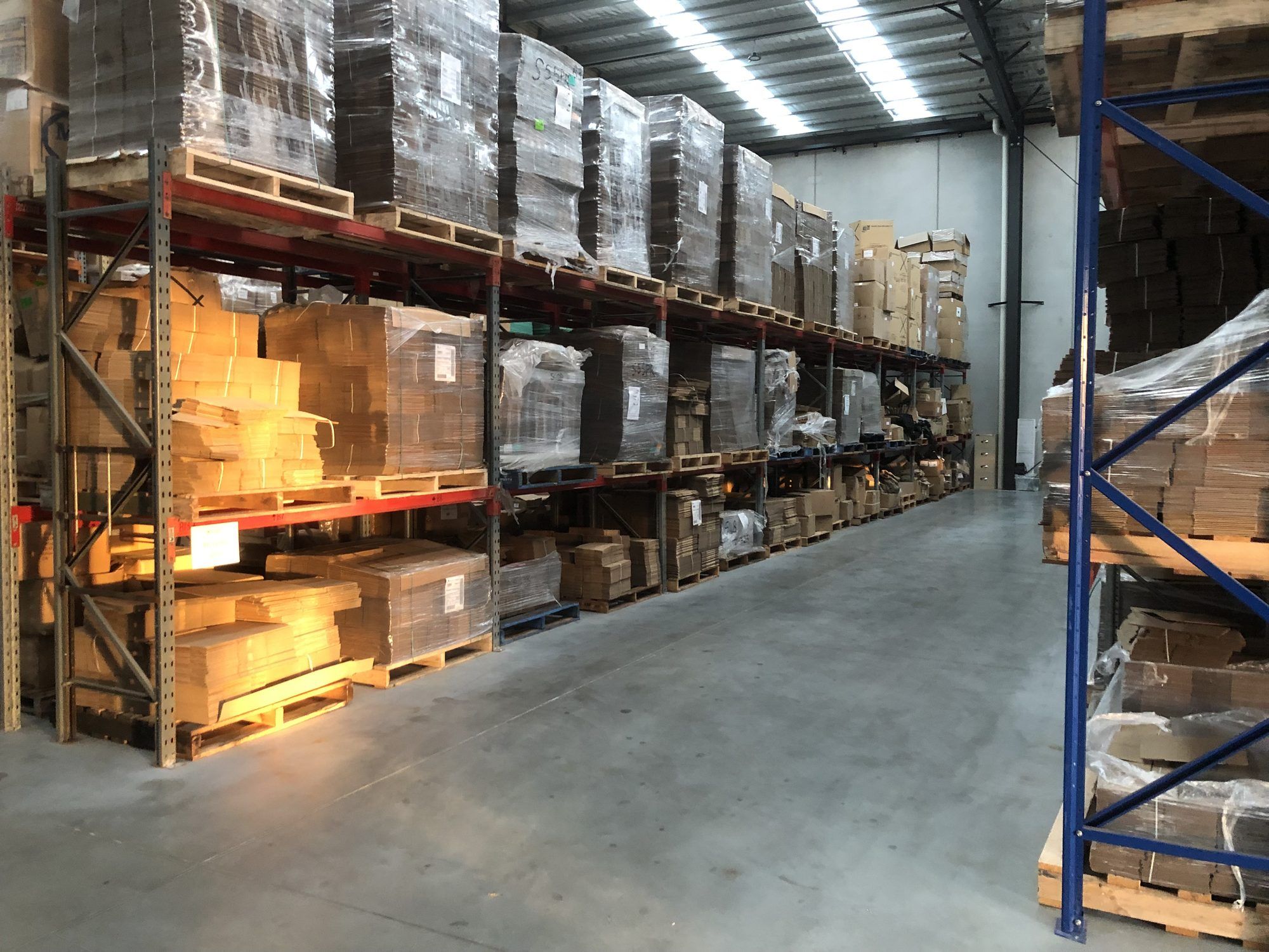 Warehouse racking stacked with flat-pack cartons and packaging components on pallets